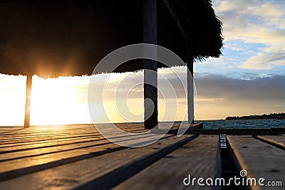 Close up of wooden gazebo on the beach at sunset or sunrise. Background of a seashore with palm trees and blue water in the early Stock Photo