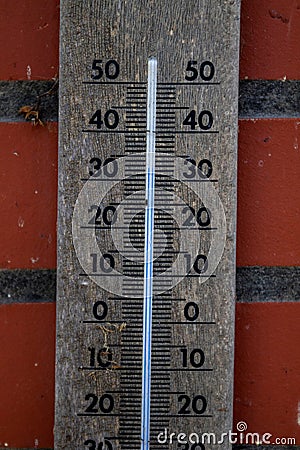 A close up of a wooden mercury thermometer indicating the outdoor temperature in degrees celcius and is hanging on a red brick Stock Photo