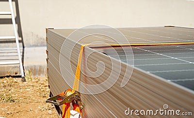 Close-up of a worker's hands tying a stack of solar panels with orange webbing Stock Photo
