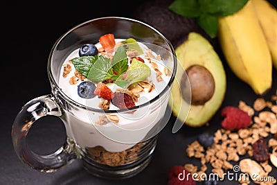 Close up yogurt with granola and fruits in glass on black granite stone Stock Photo