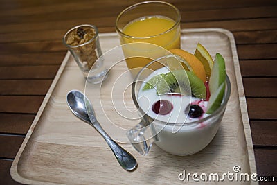 Close up of yogurt pudding in a glass with fruits decorate,honey conflake in a mug shot,orange juice in a glass on wooden plate Stock Photo