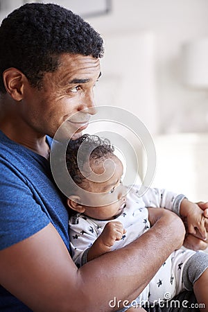 Close up of young adult African American father sitting in an armchair holding his three month old baby son, side view, waist up, Stock Photo