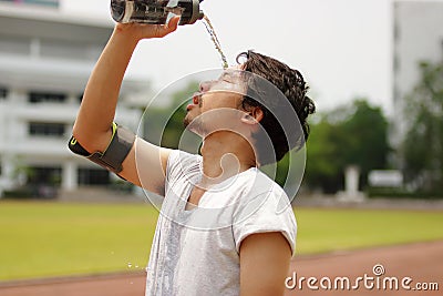 Close up young Asian runner pouring water with waterbottle on his face after running on track. Stock Photo