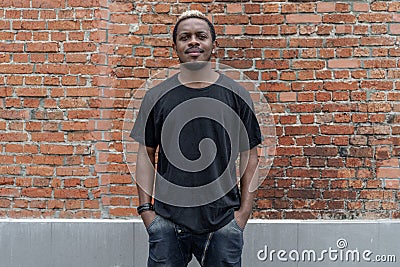Young attractive dark-skinned man in black T-shirt on red bricked background. Stock Photo