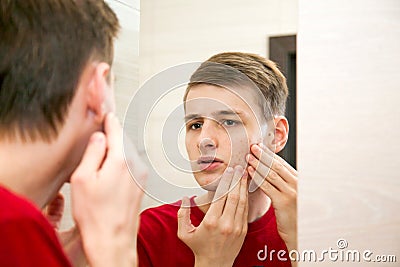 Close up of young attractive man with problematic skin and scars from acne looks in the mirror in the bathroom Stock Photo