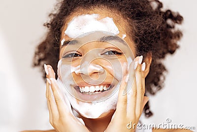 Close up of young beautiful darkskinned woman cleaning her skin with facial wash Stock Photo