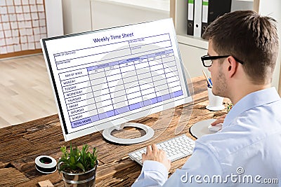Businessman Looking At Weekly Time Sheet On Computer Stock Photo