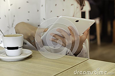 Young caucasian woman`s hands using a white tablet pc to telework while having coffee. Woman looking at multimedia Stock Photo
