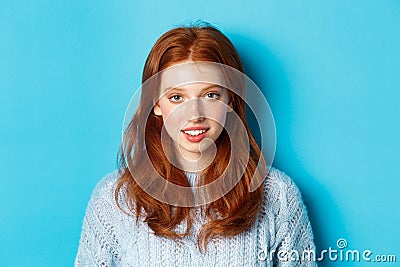 Close-up of young cute redhead girl smiling at camera, standing against blue background Stock Photo