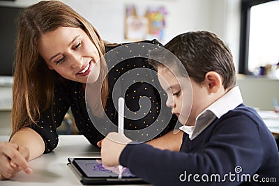 Close up of young female teacher sitting at desk with a Down syndrome schoolboy using a tablet computer in a primary school classr Stock Photo