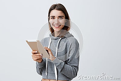 Close up of young good-looking joyful caucasian girl with dark long hair in gray sporty hoodie smiling with teeth Stock Photo