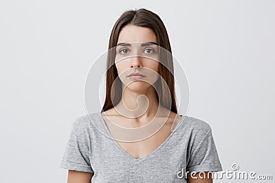 Close up of young handsome charming caucasian girl with long brown hair in gray t-shirt looking in camera with serious Stock Photo