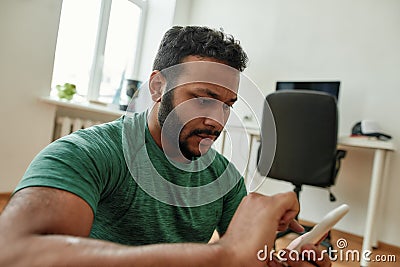 Close up of young man using smartphone app while having morning workout at home. Freshman relaxing after training Stock Photo