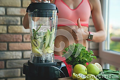 Close up of young woman with blender and green vegetables making detox shake or smoothie at home Stock Photo