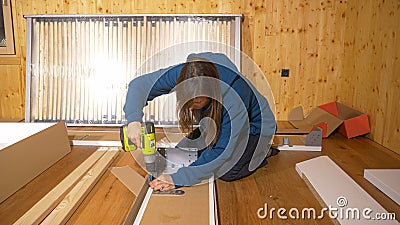 CLOSE UP: Young woman in blue hoodie assembles furniture with a power drill. Stock Photo