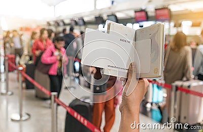 Close up of young woman holding passport and blank boarding pass at airport counters reception area with many people in background Stock Photo