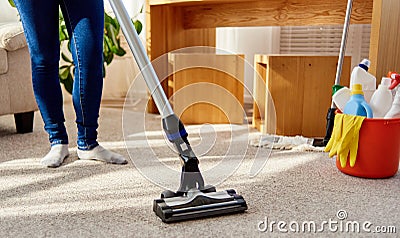 Close up of young woman in jeans cleaning carpet with vacuum cleaner in living room, copy space. Housework, household. Stock Photo