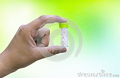 Close view image of Man hand holding a bottle of homeopathic pills over green mix yellow background Stock Photo