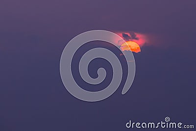 Close View Of Orange Sun Disk Partly Covered By Clouds With Crimson Glow Atop, Violet Sky Background, Sunrise, Sunset Stock Photo