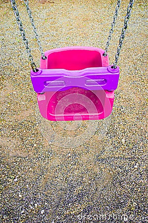 Close view of a pink plastic baby swing with purple safety bar on a playground Stock Photo