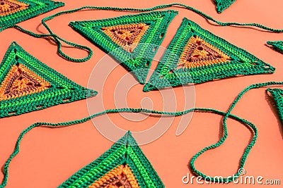 Close view of triangle crochet motifs in green and orange colors and a green crochet cord on orange background. Stock Photo