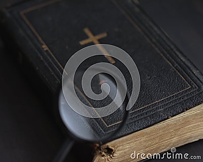 Closed ancient bible with gold cross viewed through magnifying glass. Search for truth, meaning of life. Religious book Stock Photo