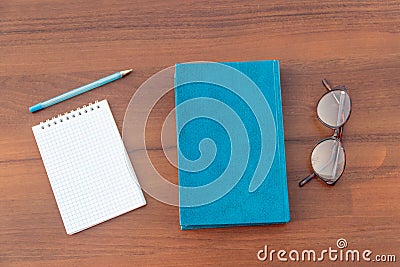 Closed book, eyeglasses, notepad and pen on wooden background Stock Photo