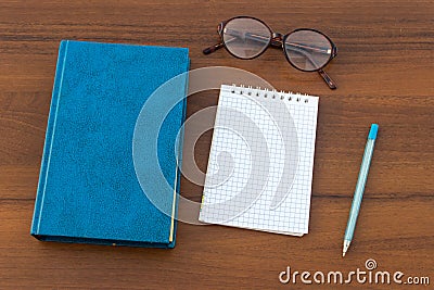 Closed book, eyeglasses, notepad and pen on wooden background Stock Photo