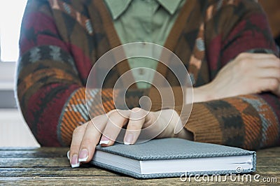 A closed book or notebook lies on a wooden table. Sitting next to a woman Stock Photo