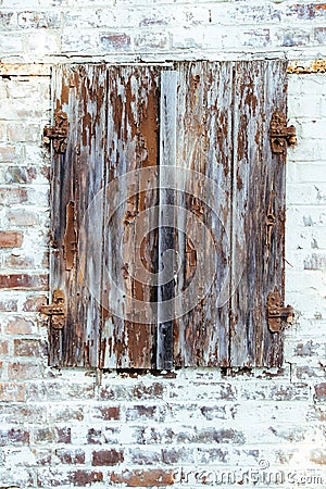 Closed brown red peeling wooden window with rusted metal hinges on a grungy white brick wall of an old abandoned derelict barn Stock Photo