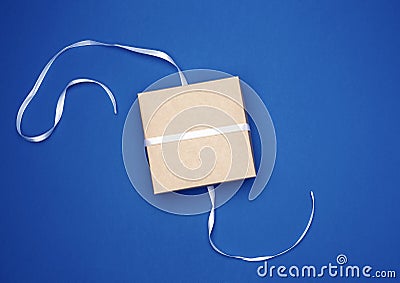 Closed cardboard gift square box tied white thin ribbon on a dark blue background Stock Photo