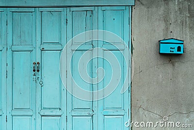 Closed green or blue wooden door and empty mail box on cracked concrete wall of house. Old home with cracked cement wall. Vintage Stock Photo