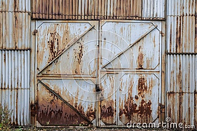 Closed old rusty iron gate sash in a corrugated iron wall. Abandoned industrial building. Grunge Stock Photo