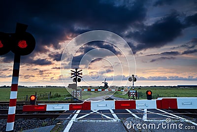 Closed rail crossing at sunrise and windmill Stock Photo