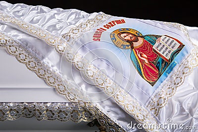 Closed wooden white coffin with white silk cloth with a picture of God. close-up on dark royal background. Stock Photo