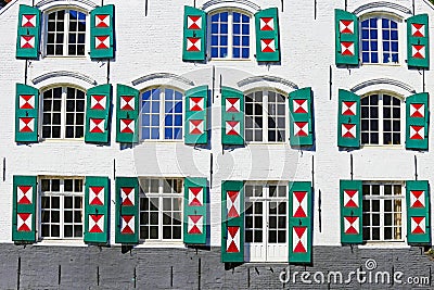 Closeup of ancient house facade, many glass windows, open exterior board batten shutters painted in triangle red white design - Stock Photo