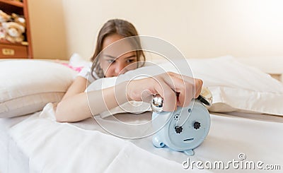 Closeup of annoyed girl reaching for alarm clock Stock Photo