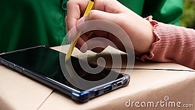 Closeup asian customer woman hand sign receipt on smartphone screen by stylus in service application and received parcel box Stock Photo
