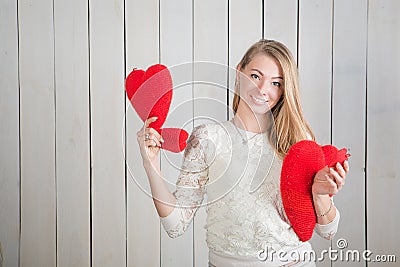 Closeup attractive blonde girl looks at camera showing many red heart shaped pillows Stock Photo