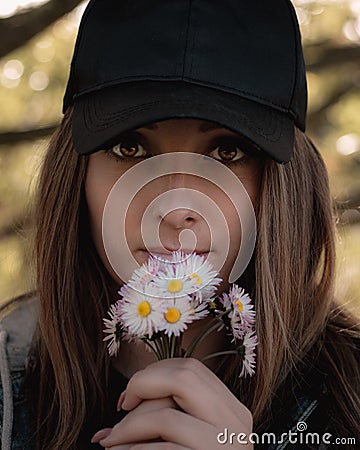 Closeup of an attractive brunette holding a bouqet of small white hand picked flowers on her lips, bright colorful amber eyes Stock Photo