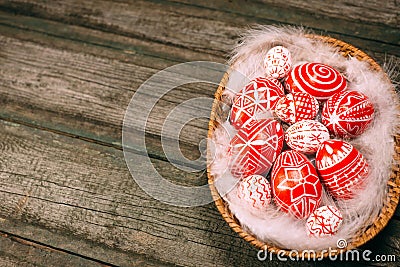 Closeup basket with Easter red eggs with folk white pattern lay on feather in the right side of rustic wood table. Ukrainian tradi Stock Photo