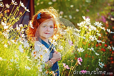 Closeup beautiful portrait ginger curly little girl in the blossoming flower garden Stock Photo