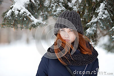 Closeup beautiful winter portrait of young adorable redhead woman in cute knitted hat winter snowy park Stock Photo