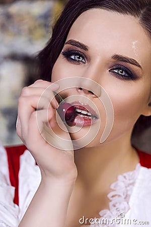 Closeup Beauty Portrait of Young Passionate Caucasian Lady in Rural Dress Posing with Red Cherry In Front of The Lips Stock Photo