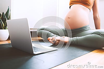 Closeup belly of pregnant woman practicing yoga online with laptop Stock Photo