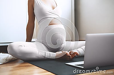 Closeup belly of pregnant woman practicing yoga online with laptop Stock Photo