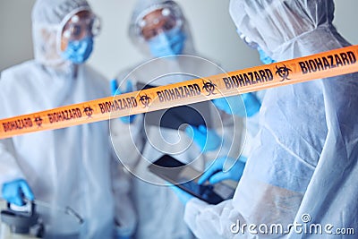 Closeup of biohazard tape blocking of prohibited area. Team of scientists cleaning prohibited area. Medical csi team Stock Photo