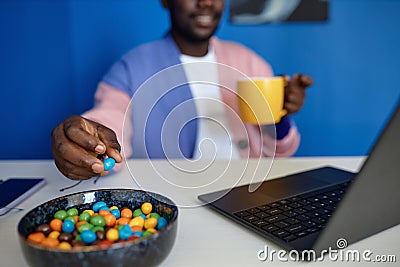 Closeup of black man enjoying candy snack and coffee in vibrant office Stock Photo