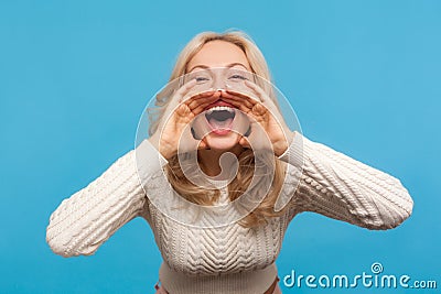 Closeup blond woman in sweater shouting holding hands near widely opened mouth, smiling and yelling splashing out emotions Stock Photo