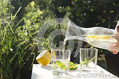 Woman poring water with lemon into glass.Refremnet time in the garden.Sunny and hot day in the garden Stock Photo